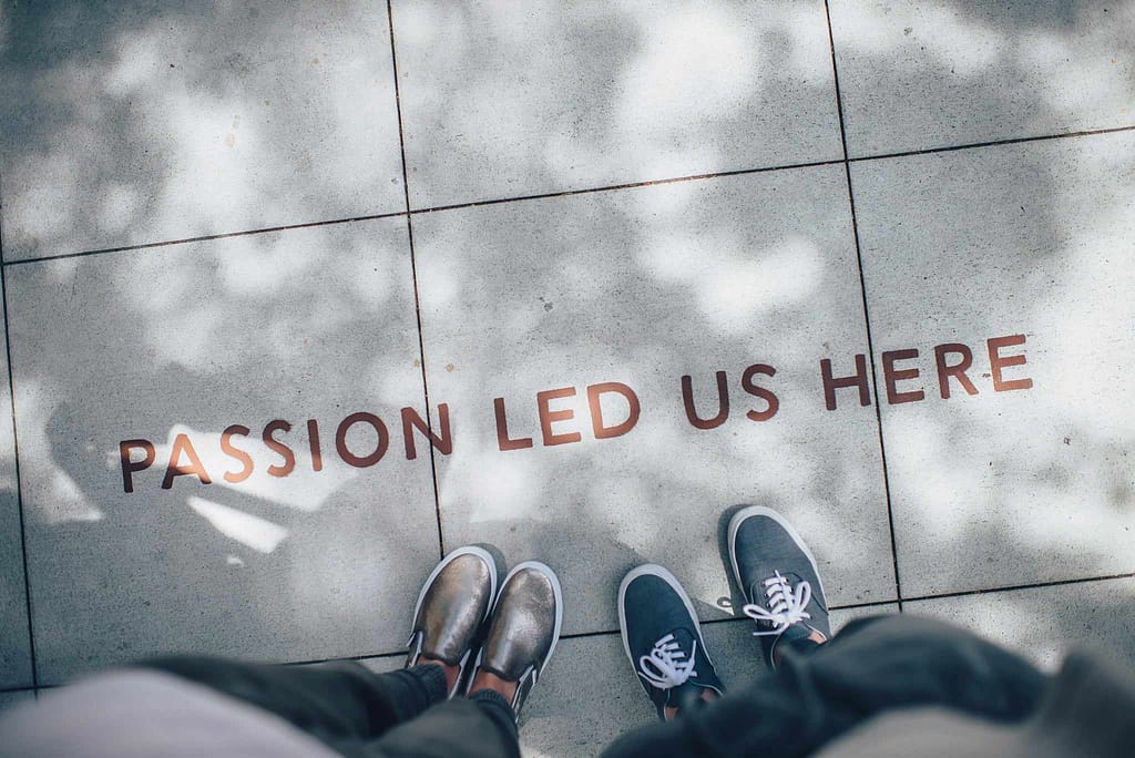image of a sidewalk from the perspective of two people looking down at their feet with the text "Passion Led Us Here" written on the sidewalk